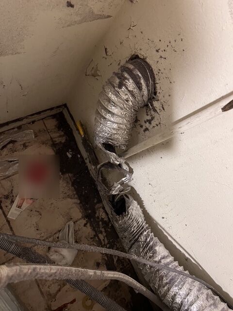 Crushed, torn foil dryer hose with lint behind a dryer